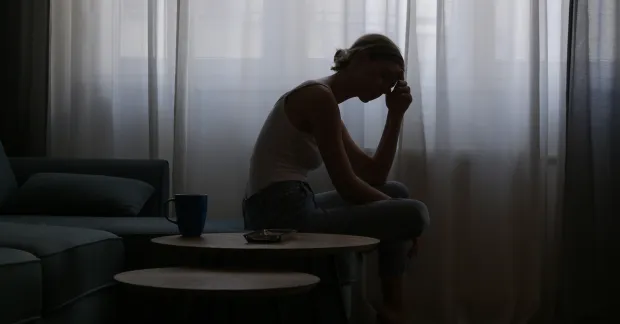 kvinna sitter i ett mörkt rum och tar sig för huvudet