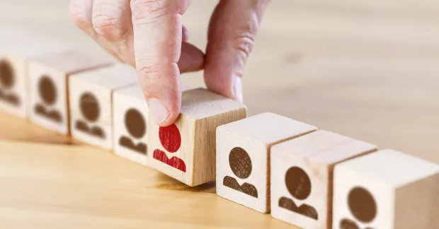 Små klossar med personer på och en hand som tar upp en kloss. 