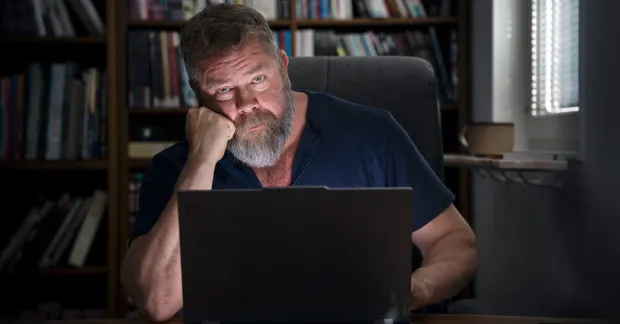 Ghostning vid rekrytering. Jörn Green sökte hundratals jobb utan att få svar. Sitter vid en dator i ett mörkt rum, skäggig, ser allvarlig ut.