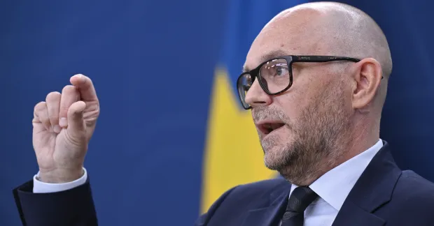 Arbetsmarknadsminister Johan Britz i kostym visar på något litet mellan tumme och pekfinger.