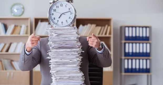 Pappershög på skrivbord och en klocka