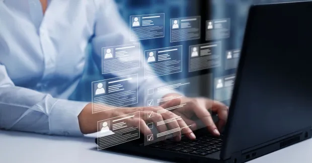 Person som skriver på en laptop med digitala profiler och checklistor ovanpå skärmen, symbol för bakgrundskontroller vid rekrytering.