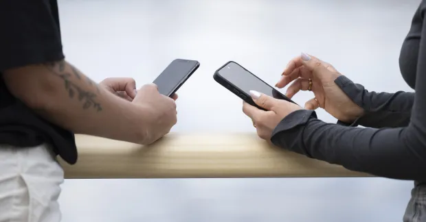 Två personer står med varsin mobiltelefon under en paus. Bilden illustrerar phubbing på jobbet och hur mobilanvändning kan påverka samtal mellan kollegor.