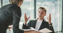 Kvinna visar papper för gestikulerande man på kontor.