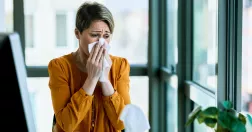 Kvinna på kontor snyter sig och ser besvärad ut.