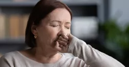 Kvinna ser ansträngd ut och för näven mot munnen.