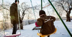 Vinterlandskap. En pappa gungar sitt barn. 