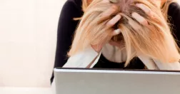 Kvinna framför dator. Håller huvudet i händerna. Är stressad. 