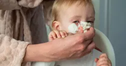 Ett litet barn får näsan torkad av en vuxen person. Bilden illustrerar vab och vård av sjukt barn.