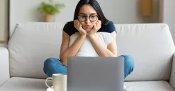 Kvinna sitter i soffan med huvudet i händerna framför laptop.