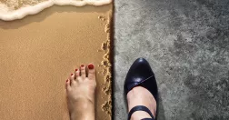Kvinna står med ena foten barfota på en strand och den andra i en klacksko på ett golv.