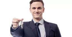 Manlig mäklare håller upp ett par nycklar och ler.