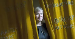 Marika Markovits kikar fram mellan gula drapperier.