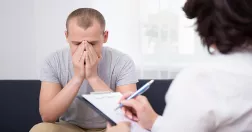 Man sitter med nedböjt huvud i samtal med kvinna som antecknar.