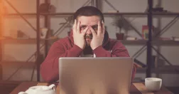 Man vid dator tar sig för ansiktet.