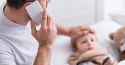 Man talar i telefon håller handen på ett sängliggande barn.