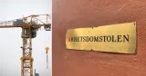 Till vänster en byggkran. Till höger en skylt med texten Arbetsdomstolen. 