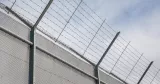 Fängelsestängel med taggtråd mot grå himmel.