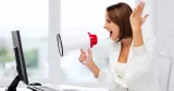 Konflikthantering i arbetslivet. En kvinna på kontor skriker i megafon mot sin dator.