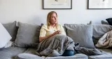 Hemmiljö med Jeanette Lilja i soffa och filt. Illustrerar situationen när barnet blir hemmasittare och vardagen stannar hemma.