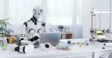 Robot sitter vid en laptop på ett kontor, som illustration till AI på arbetsplatsen och hur tekniken kan påverka tjänstemannajobb.