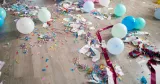 Ballonger, färgad konfetti, serpentiner och sönderrivet papper ligger utspridda på ett ljust golv efter en fest.