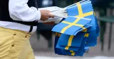 Man iförd folkdräkt bär på svenska flaggor.