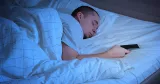 Man ligger och sover med mobilen i handen.